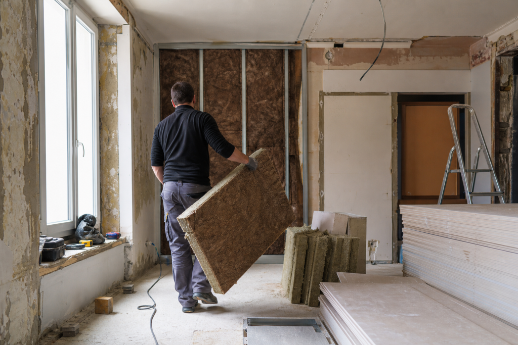 ouvrier portant panneau d'isolation dans pièce en rénovation
